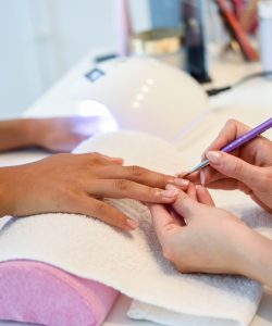 Close-up of beautician painting a woman's nails with a brush in a nail salon. Costumer receiving a manicure.